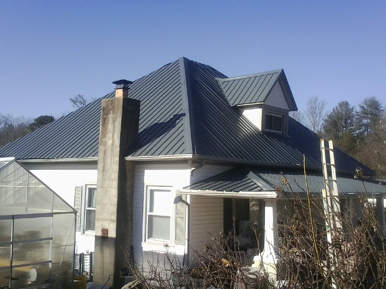 Dark blue standing seam metal roof on a white farmhouse with dormer — Slate & Tile Roof Repair by Roofing Brothers in Cardwell