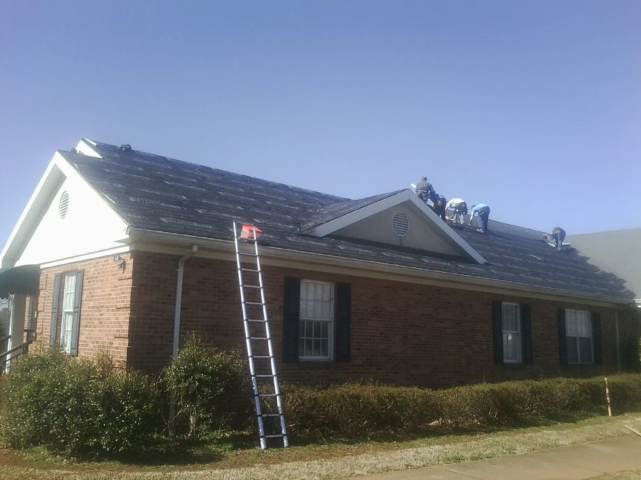 Crew tearing shingles off a brick ranch roof with a ladder set — Emergency Roof Repair work by our crew in Cardwell