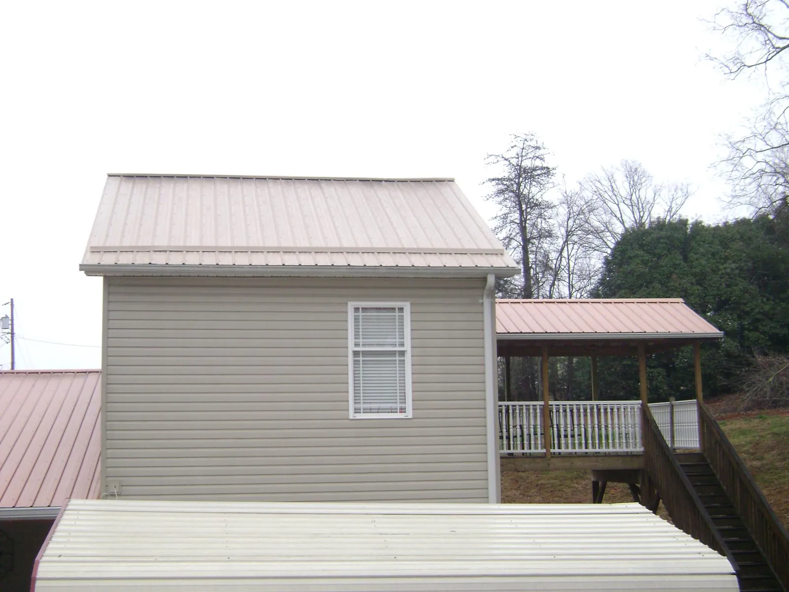 Tan metal roofs on a two story addition and attached porch, from a Roof Replacement job in Cardwell